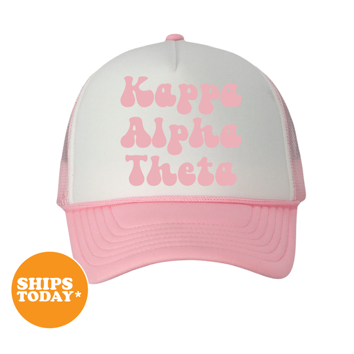 A pink and white baseball cap with the text "KaPPe Alpha Theta" printed on it.