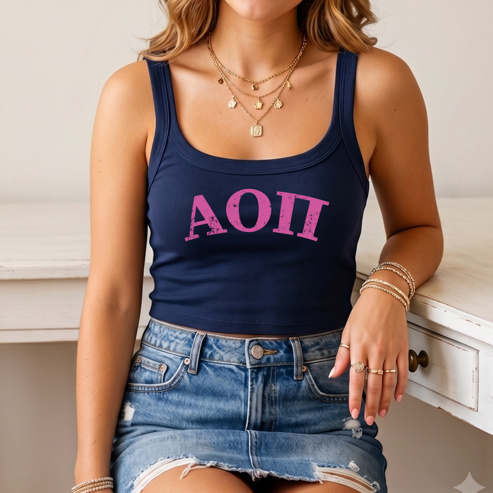 A woman wearing a navy blue crop top with the letters "AOI" printed in pink, denim shorts, and multiple rings on her fingers.