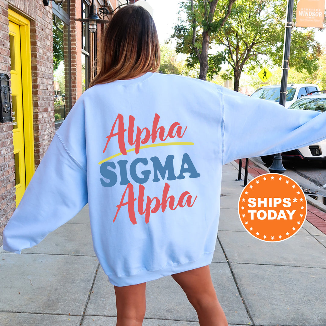 A woman wearing a light blue sweatshirt with the text "Alpha Sigma Alpha" printed on it, standing on a sidewalk.