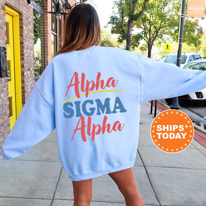 A woman wearing a light blue sweatshirt with the text "Alpha Sigma Alpha" printed on it, standing on a sidewalk.