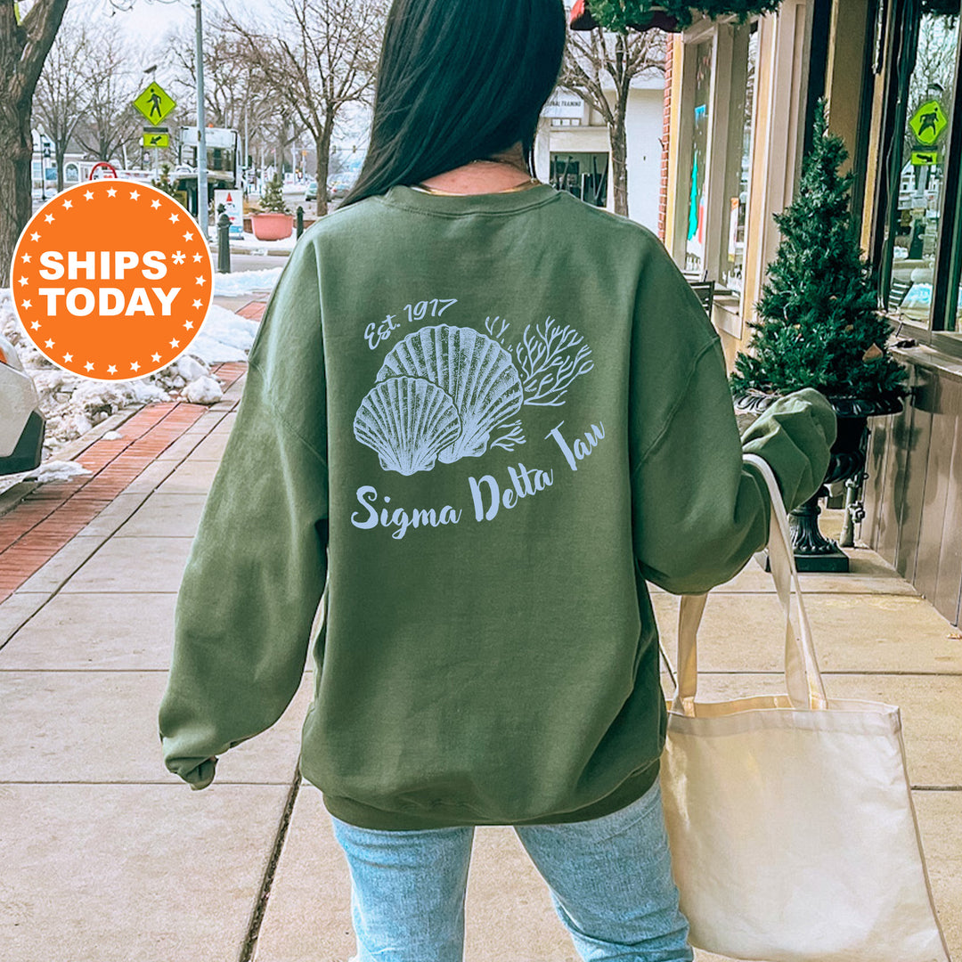 A woman wearing a green sweatshirt with a graphic design of a shell and the text "Sigma Delta Taw" is walking down a city street.