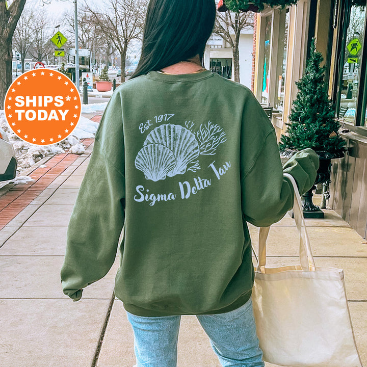 A woman wearing a green sweatshirt with a graphic design of a shell and the text "Sigma Delta Taw" is walking down a city street.