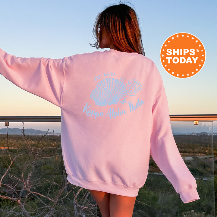 A woman wearing a pink sweatshirt with a graphic design on the back, standing on a balcony overlooking a scenic landscape.