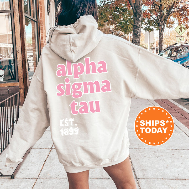 A person wearing a white hoodie with pink text and a logo, standing on a sidewalk.