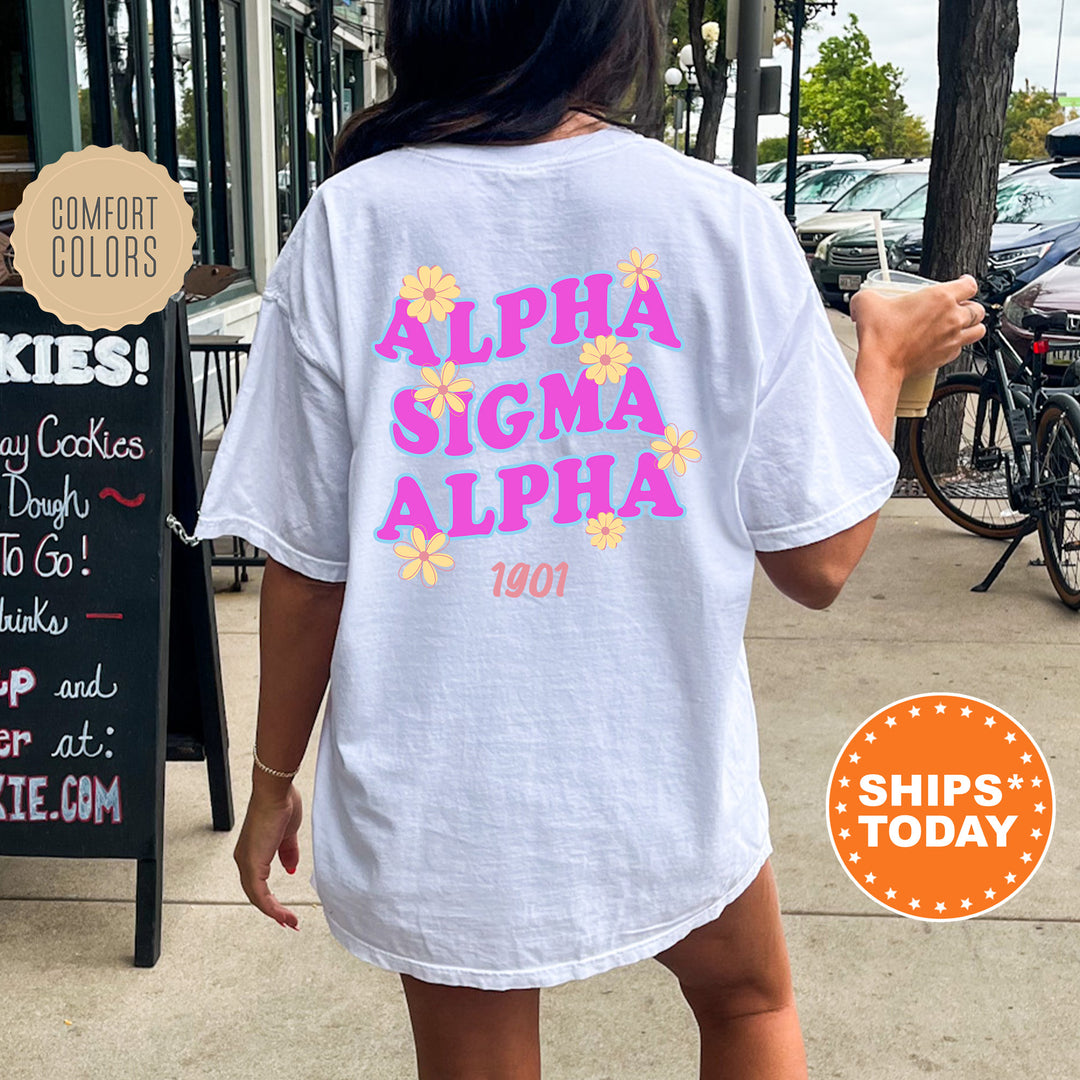 A person wearing a white t-shirt with the text "ALPA SIGMA ALPHA 1901" printed on it, standing on a sidewalk next to a chalkboard sign.