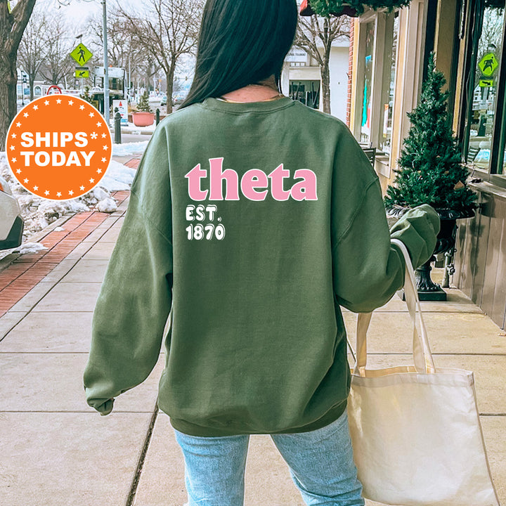 A person wearing a green sweatshirt with the text "theta EST. 1870" printed on it, walking on a sidewalk.