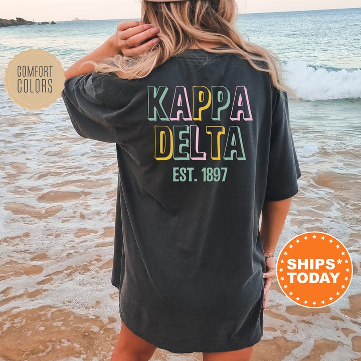 a woman standing on the beach wearing a black kapa delta shirt