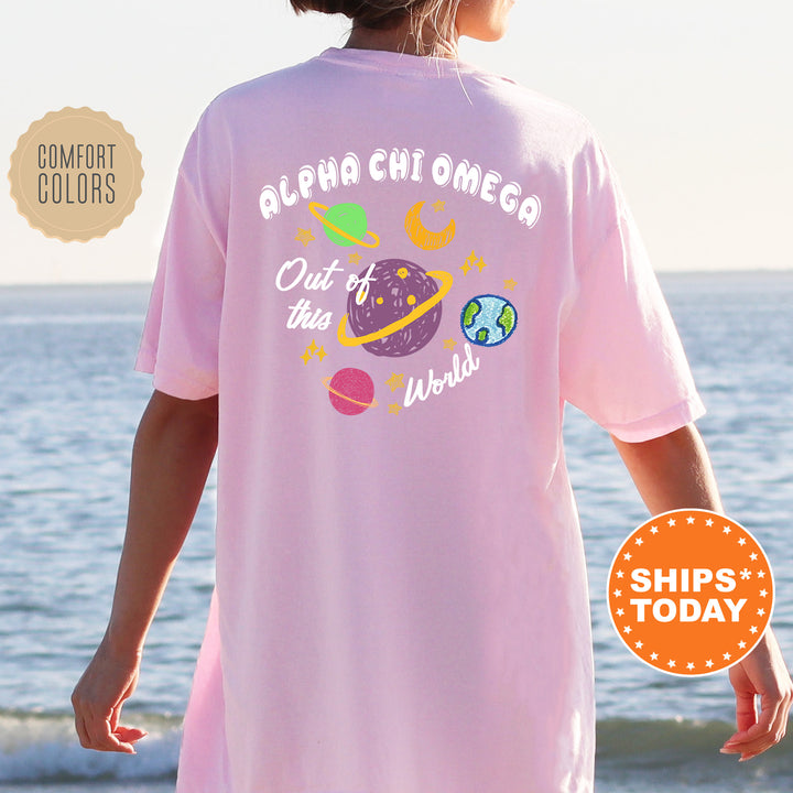A person wearing a pink t-shirt with a graphic design of planets and stars, standing near the ocean.