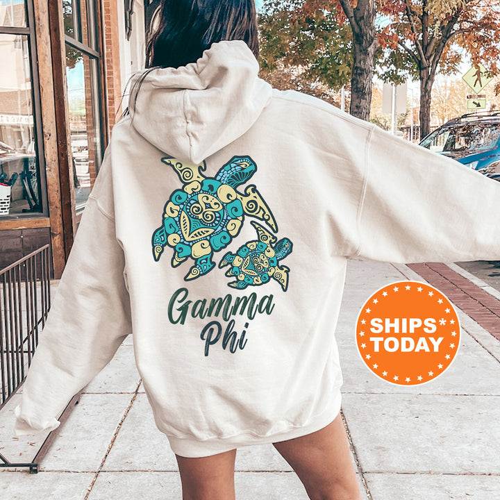 A person wearing a white hoodie with a graphic of a turtle and the text "Gamma Phi" printed on it, standing on a sidewalk.