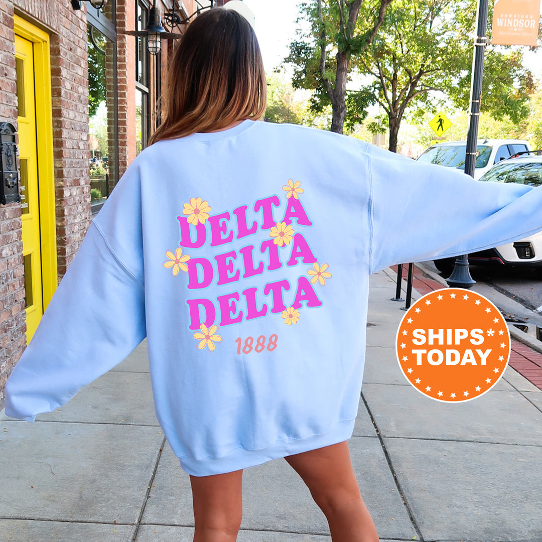 A woman wearing a light blue sweatshirt with the text "DELTA DELTA" and "1888" printed on it, standing on a sidewalk.