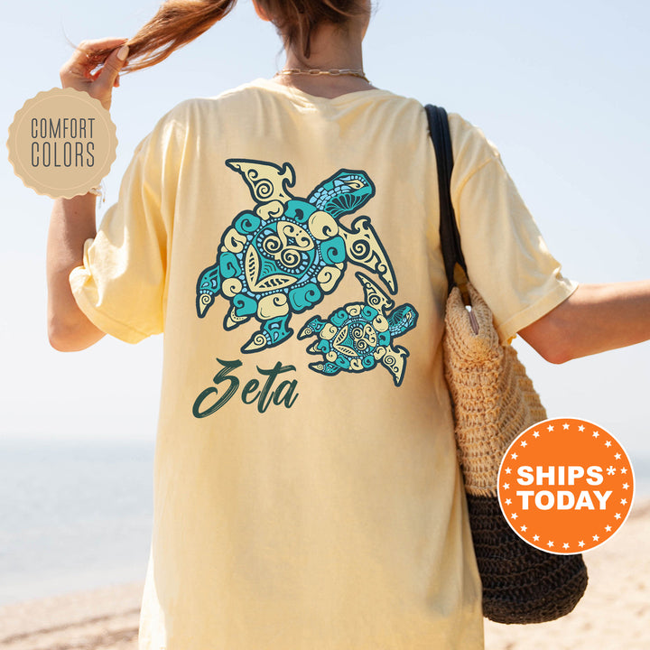 A person wearing a yellow t-shirt with a turtle design and the word "Zeta" printed on it, standing on a beach.