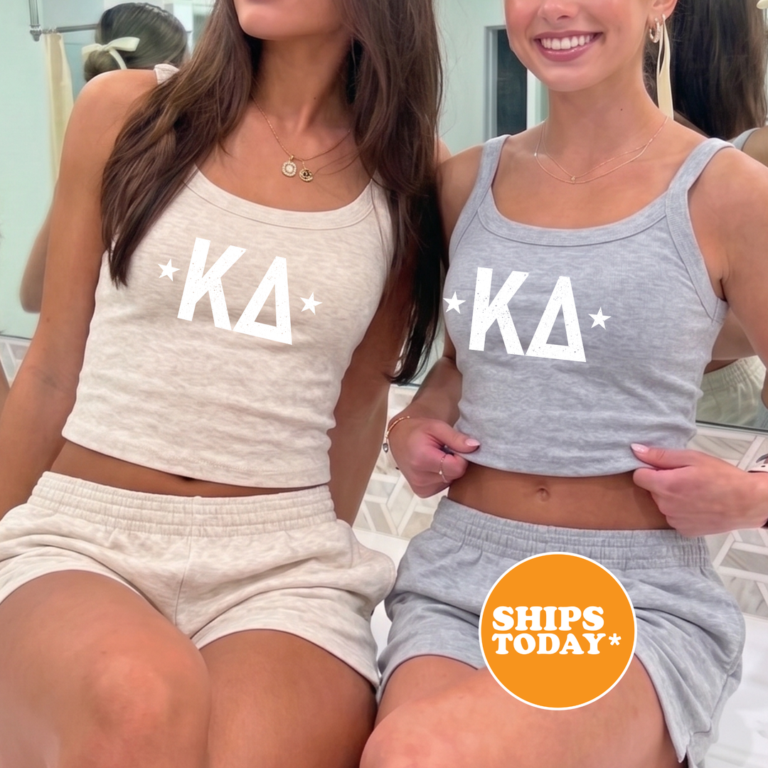 Two women wearing matching gray tank tops with white letters and stars, posing together in front of a mirror.