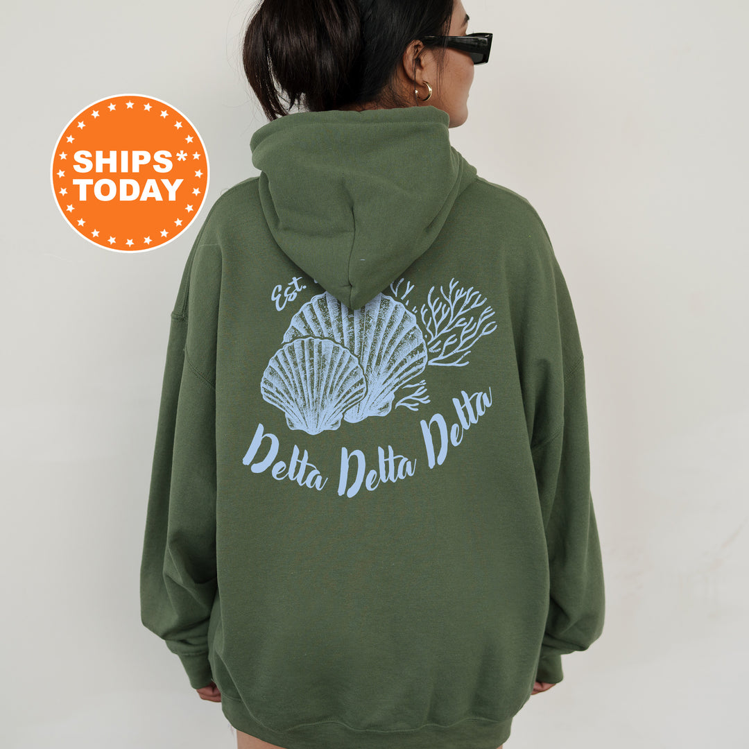 A person wearing a green hoodie with a graphic of seashells and the text "Delta Delta Delta" printed on the back.