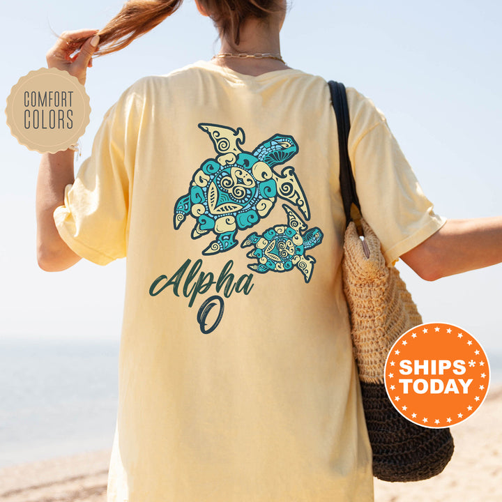 A person wearing a yellow t-shirt with a turtle design and the word "Alpha" printed on it, standing on a beach.