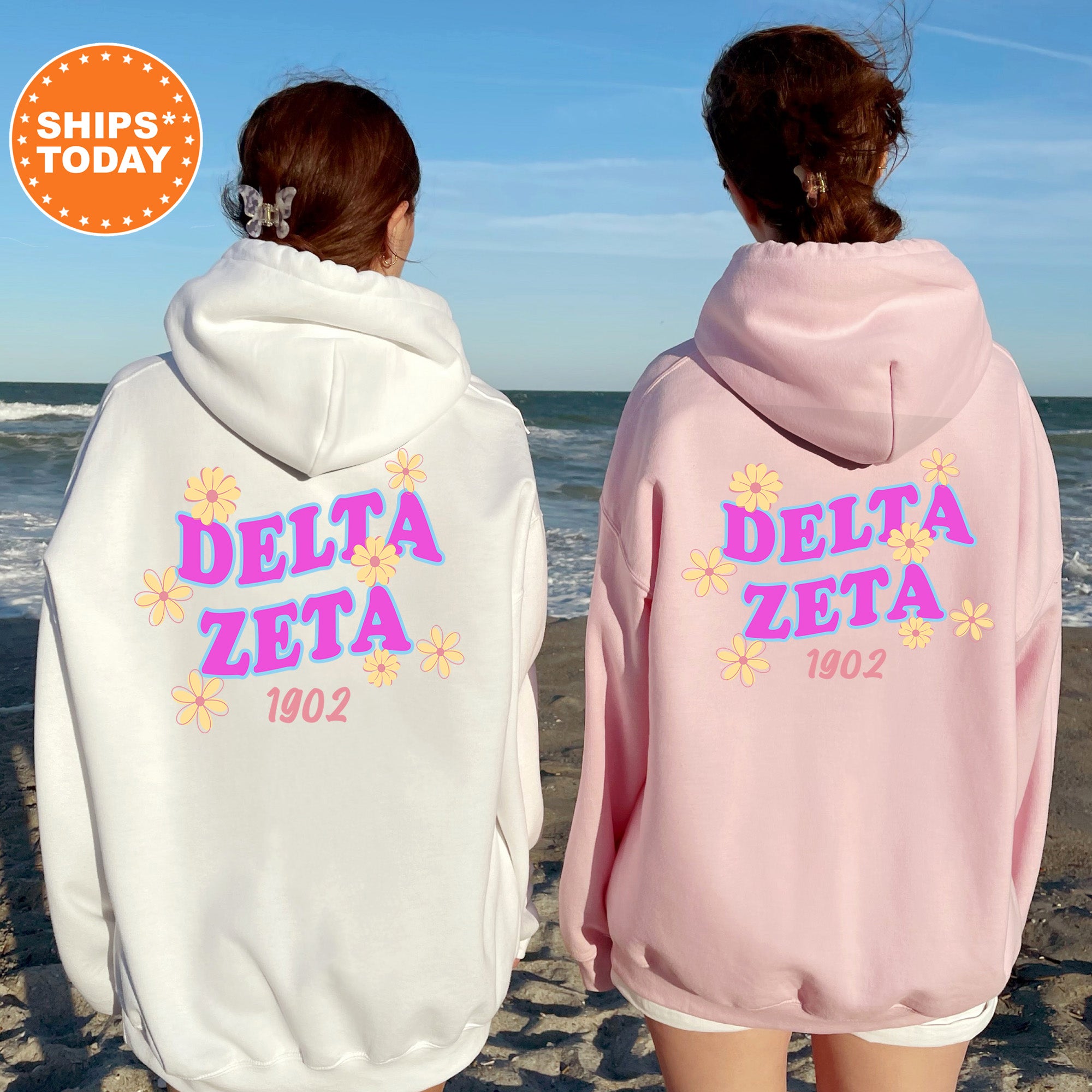 Two women wearing hooded sweatshirts with the Delta Zeta logo standing on a beach.