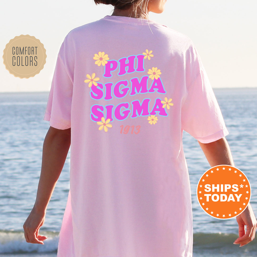 A person wearing a pink t-shirt with the text "PHI SIGMA SIGMA 1913" printed on it, standing near the ocean.