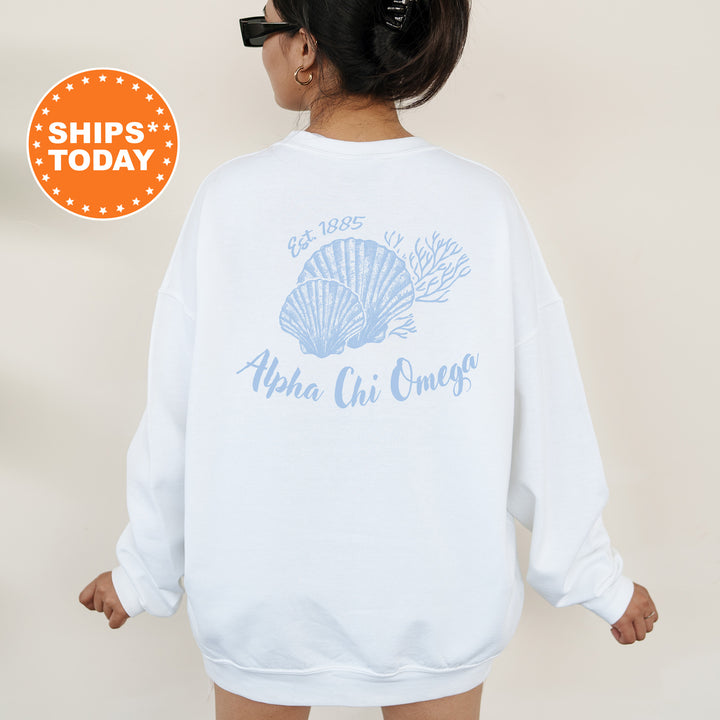 A woman wearing a white sweatshirt with a graphic design of a shell and the text "Alpha Chi Omega" printed on it.
