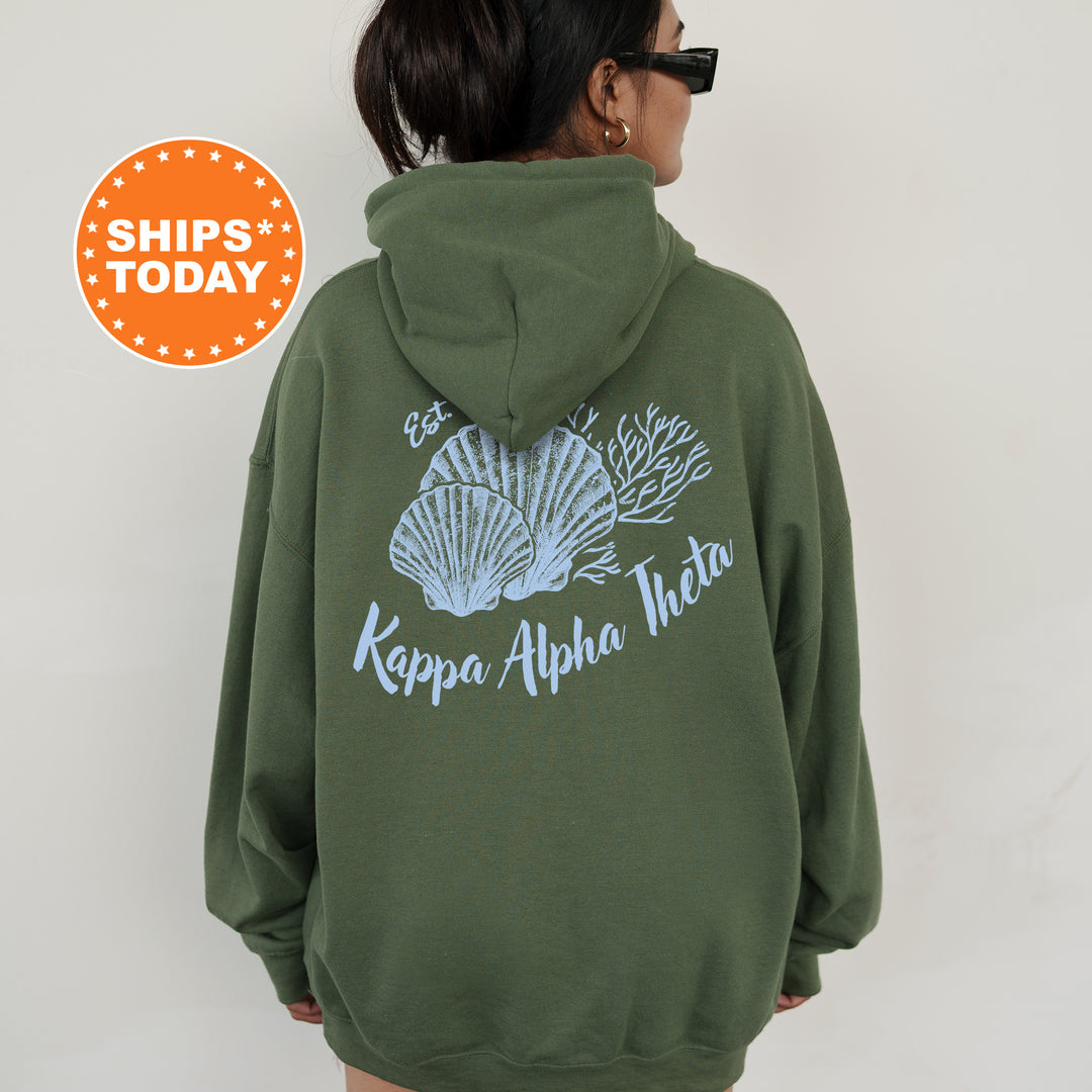 A person wearing a green hoodie with a graphic design of seashells and the text " Kappa Alpha Theta" printed on the back.
