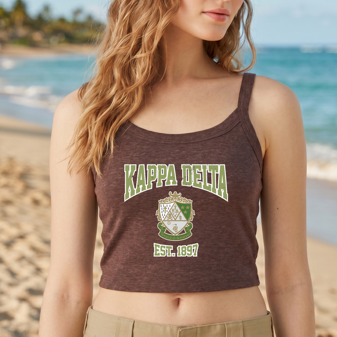 A woman wearing a brown tank top with the text "Kappa Delta EST. 1847" printed on it, standing on a beach with the ocean in the background.