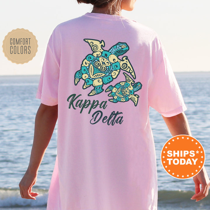 A person wearing a pink t-shirt with a graphic of a turtle and the text "Kappa Delta" printed on it, standing near the ocean.
