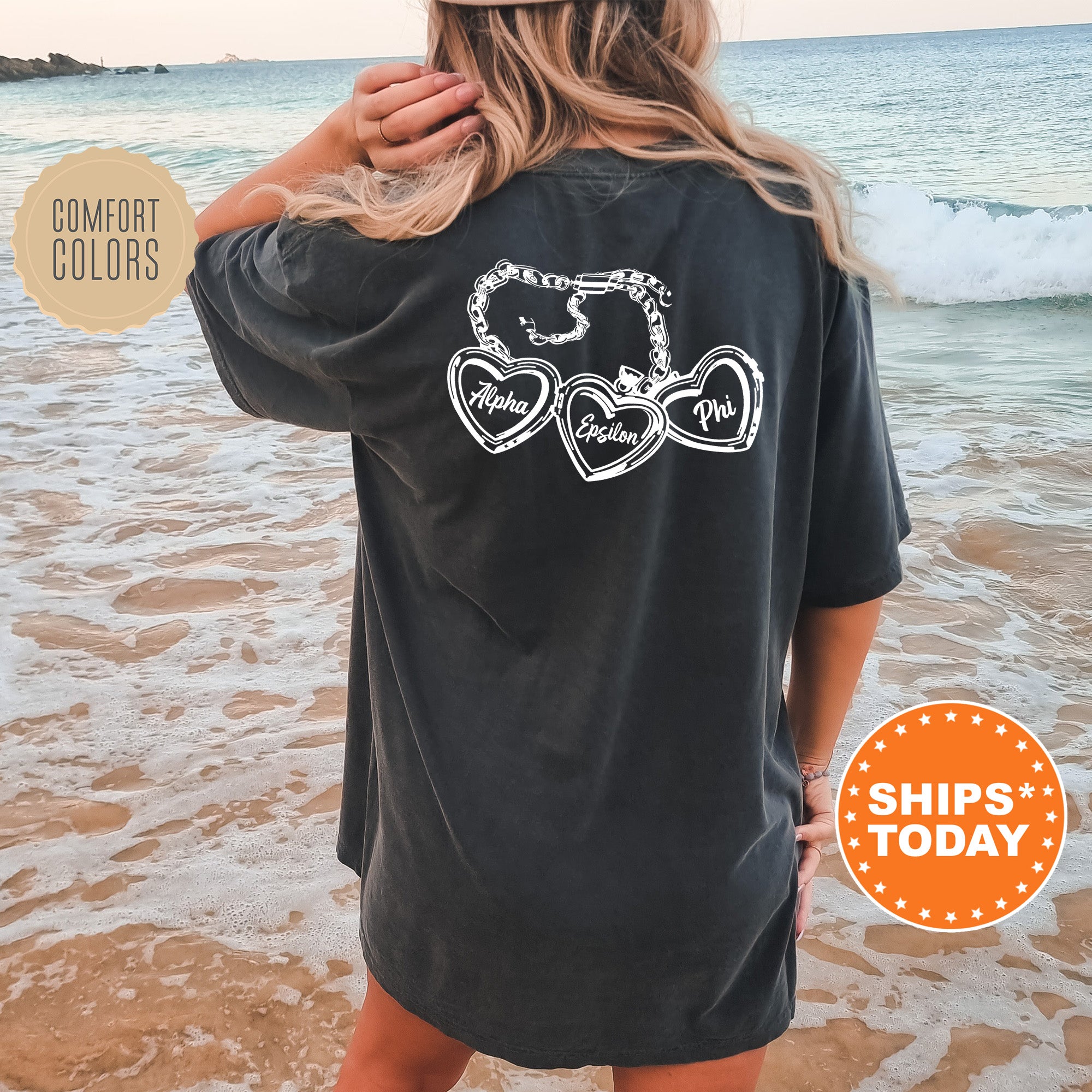 A woman wearing a black t-shirt with a graphic design on the back is standing on a beach, with the ocean visible in the background.