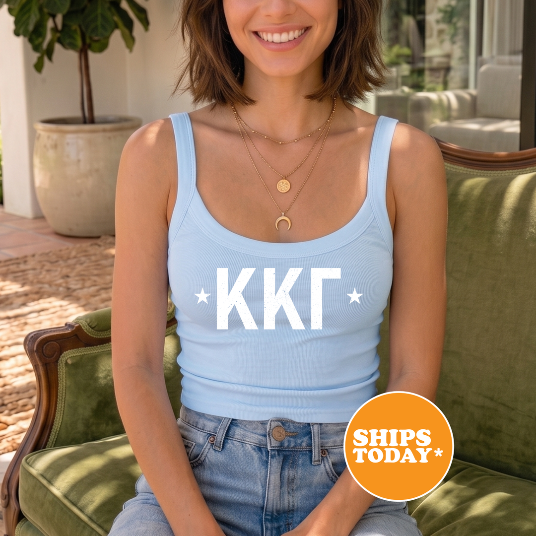 A woman wearing a light blue tank top with white text and a crescent moon design, sitting on a green chair.