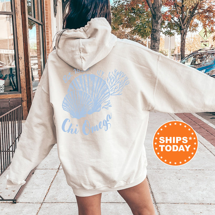 A person wearing a white hoodie with a blue design and text on the back is standing on a sidewalk.