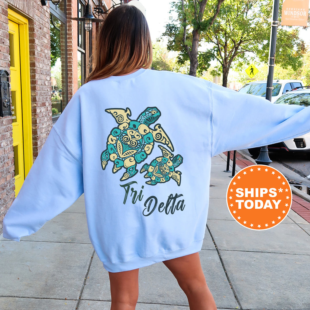 A woman wearing a light blue sweatshirt with a turtle design and text on the back, standing on a sidewalk.