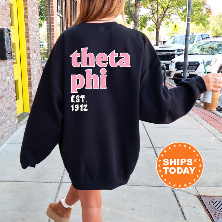 A person wearing a black sweatshirt with pink text and a logo, walking on a sidewalk.