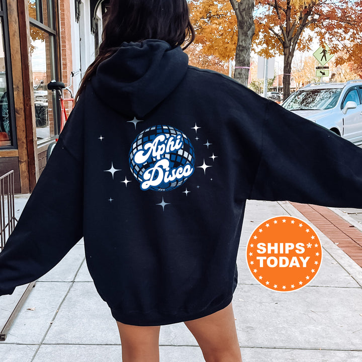 A person wearing a black hoodie with a graphic design on the back, standing on a sidewalk with a street and trees in the background.