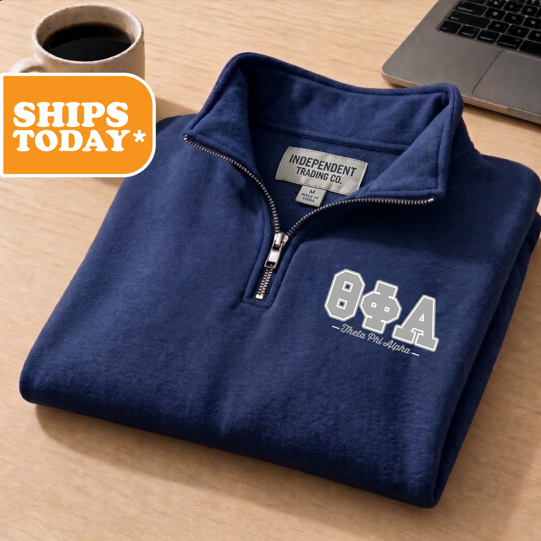 A navy blue sweatshirt with a zipper and a logo on the front, placed on a wooden surface next to a laptop and a coffee cup.