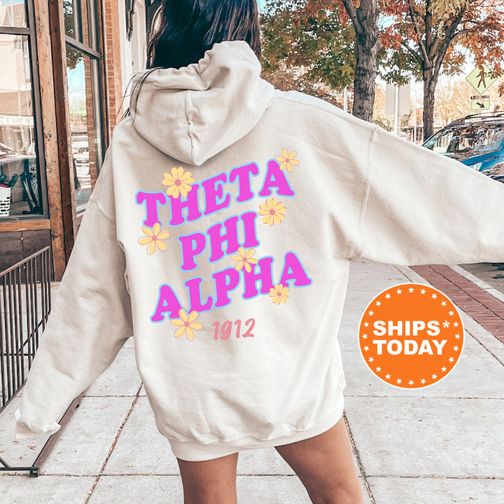 A person wearing a white hoodie with the text "THETA PHI ALPHA" printed on it, standing on a sidewalk.