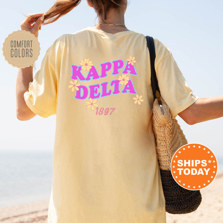 A woman wearing a yellow t-shirt with the text "KAPPADELTA" and " 1897" printed on it, standing on a beach.