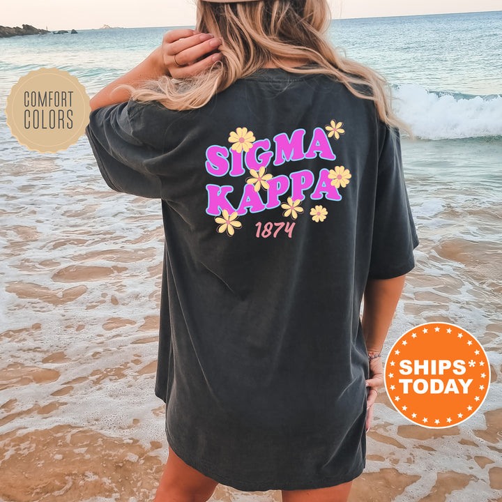 A woman wearing a black t-shirt with the text "SIGMA KAPPAS 1874" printed on it, standing on a beach with the ocean in the background.