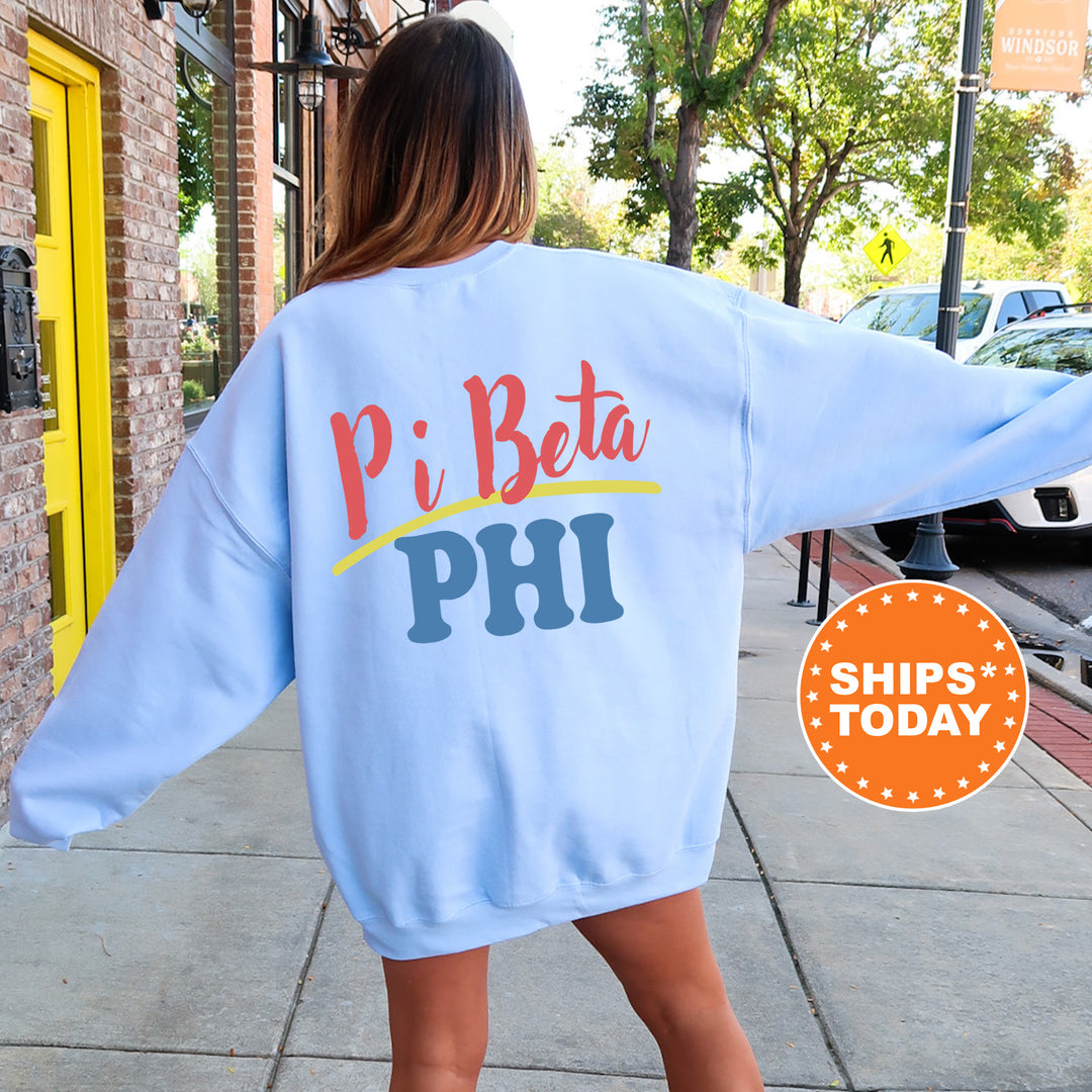 A woman wearing a light blue sweatshirt with the text "Pi Beta Phi" printed on it, standing on a sidewalk.