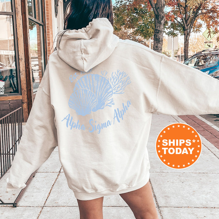A person wearing a white hoodie with a blue shell design and text on the back is standing on a sidewalk.
