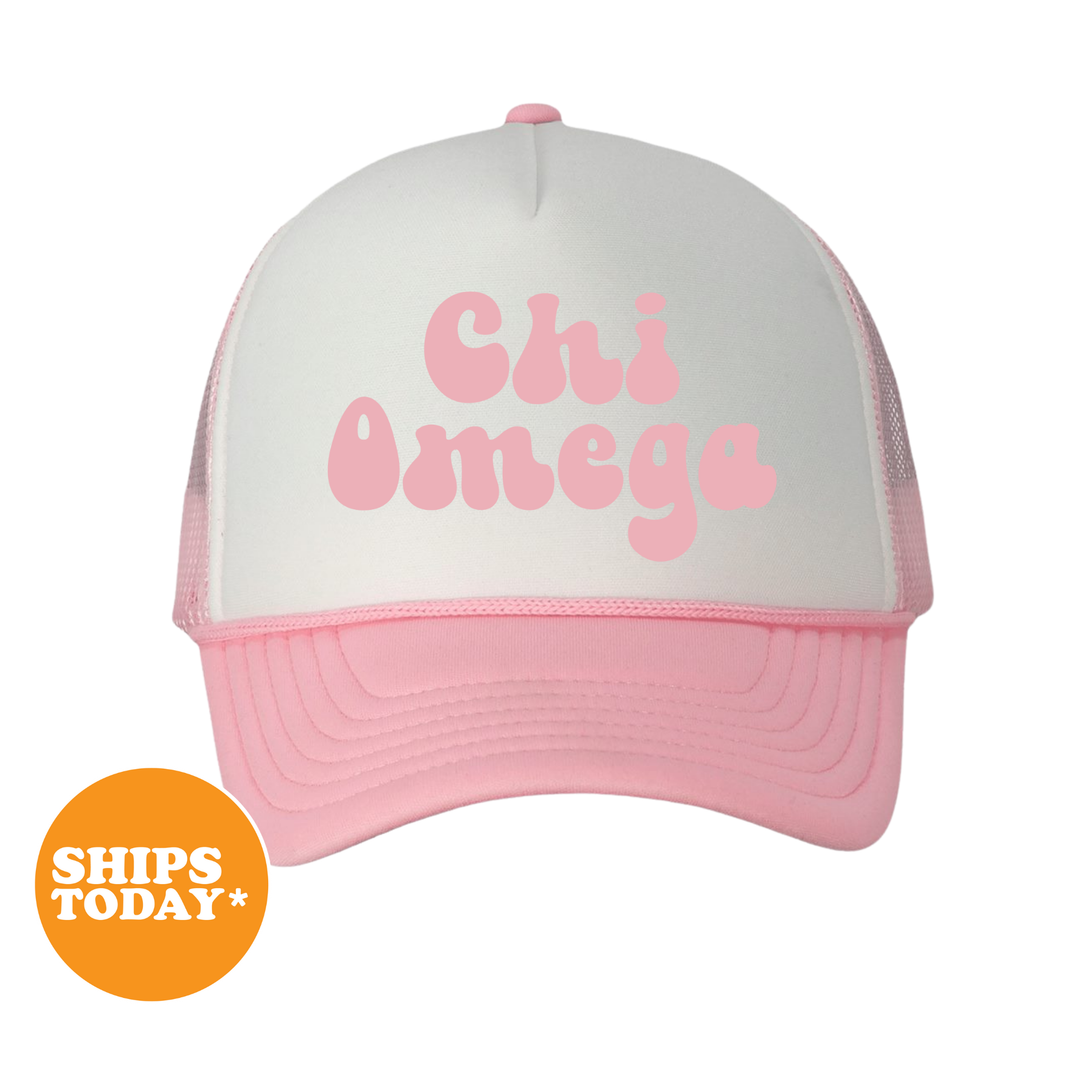 A pink and white baseball cap with the text "Chi Omega" printed on it.
