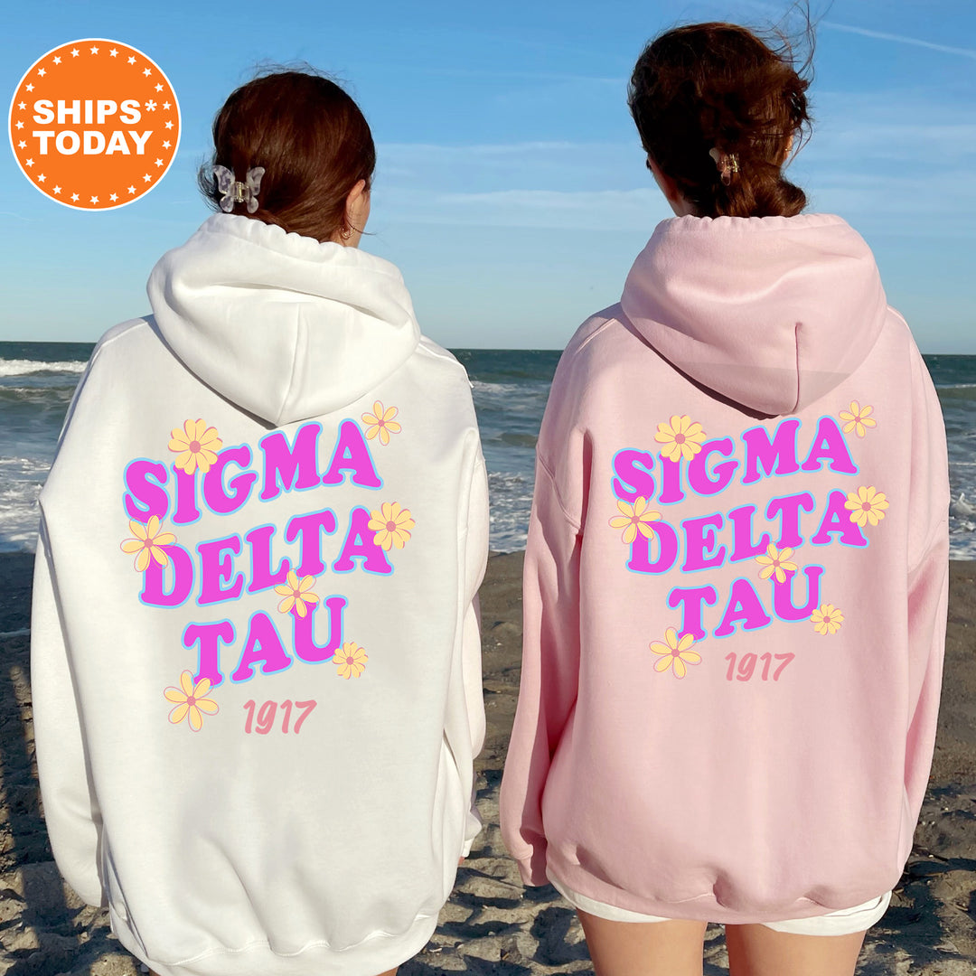 Two women wearing matching Sigma Delta Tau hoodies stand on a beach, facing the ocean.