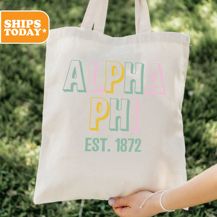 a person holding a tote bag with the words alpha phi on it