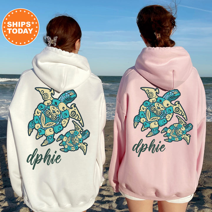 Two women wearing hooded sweatshirts with a turtle design on the back, standing on a beach with the ocean in the background.
