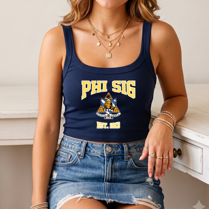 A woman wearing a navy blue crop top with the text "PHI SIG EST. 1983" printed on it, paired with a denim skirt and multiple rings on her fingers.