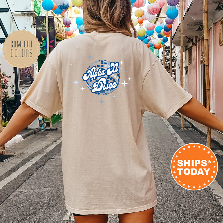 A person wearing a beige t-shirt with a graphic design on the back, standing on a street with colorful lanterns hanging overhead.