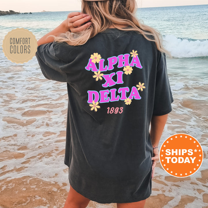 A woman wearing a black t-shirt with the text "ALPHA XI DELTA" printed on it, standing on a beach with the ocean in the background.
