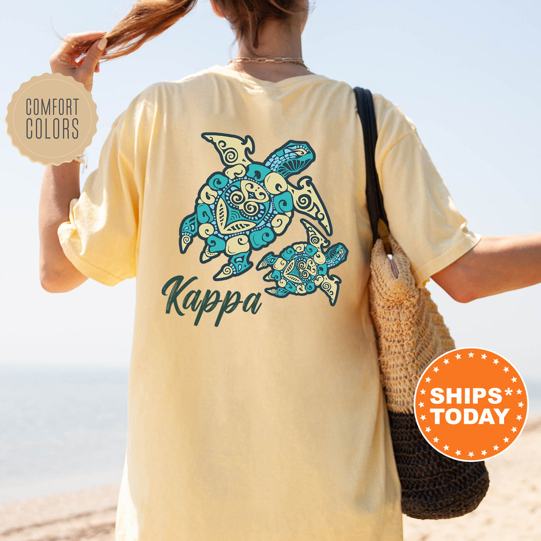 A person wearing a yellow t-shirt with a turtle design and the word "Kappa" printed on it, standing on a beach.