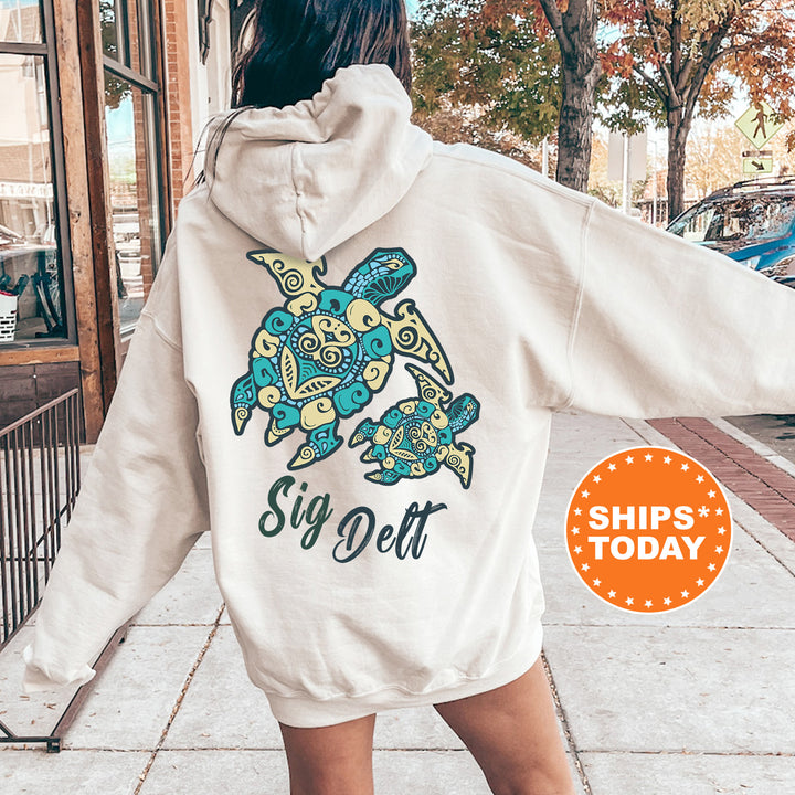 A person wearing a white hoodie with a colorful turtle design and the text "Sign Delt" printed on it, standing on a sidewalk.