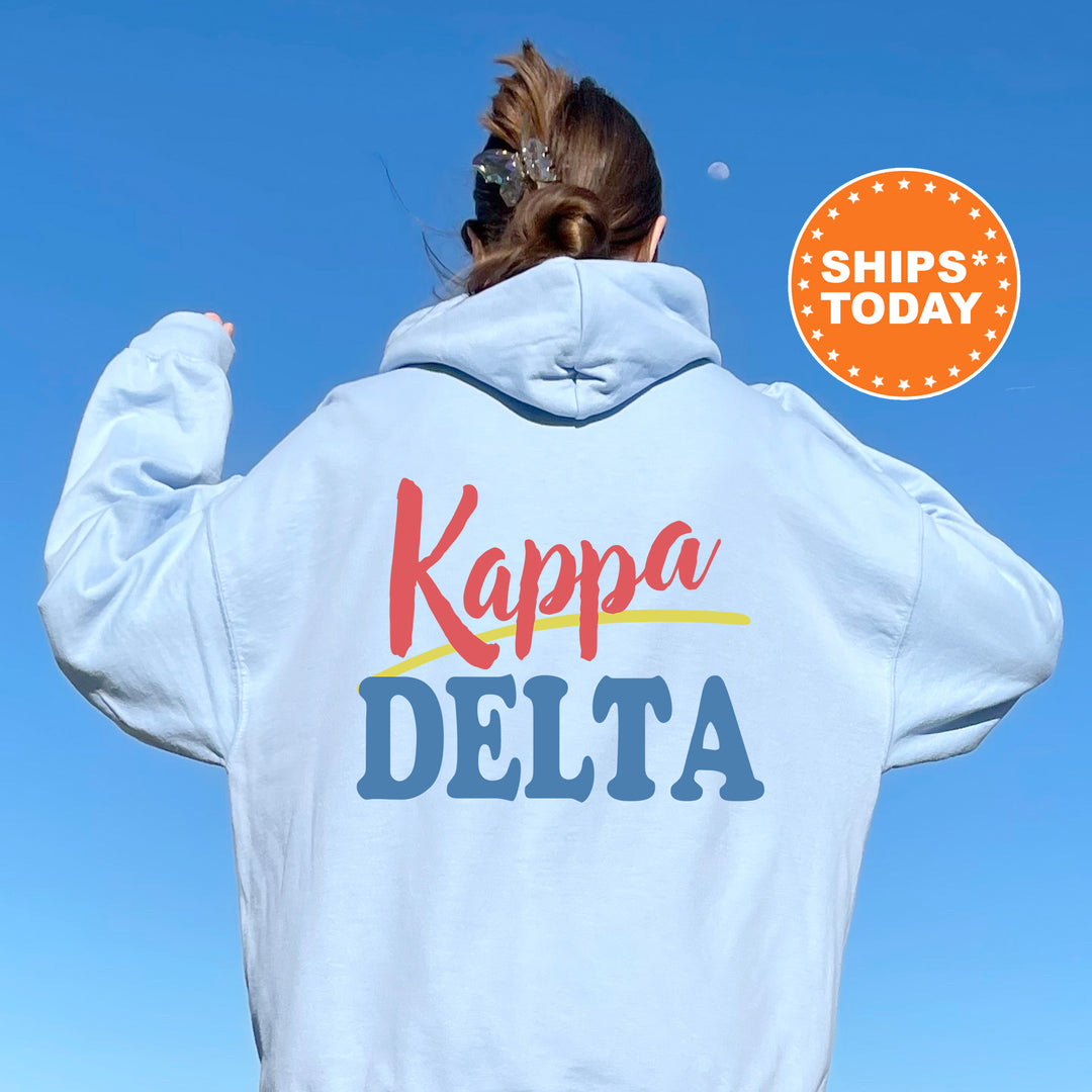 A person wearing a white hoodie with the text "Kappa Delta" printed on it, standing against a clear blue sky.