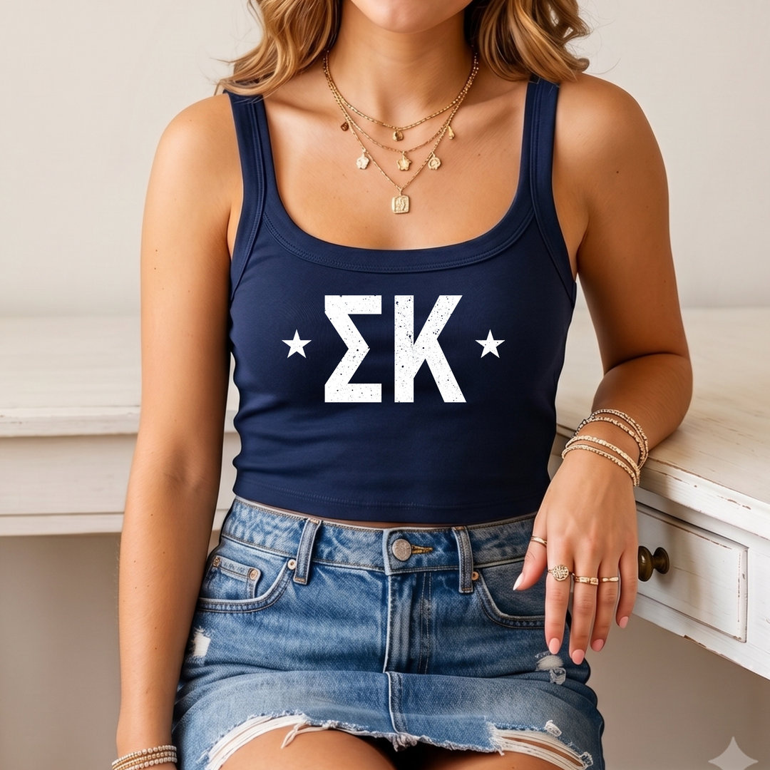A woman wearing a navy blue crop top with white text and a denim skirt, sitting on a white surface.