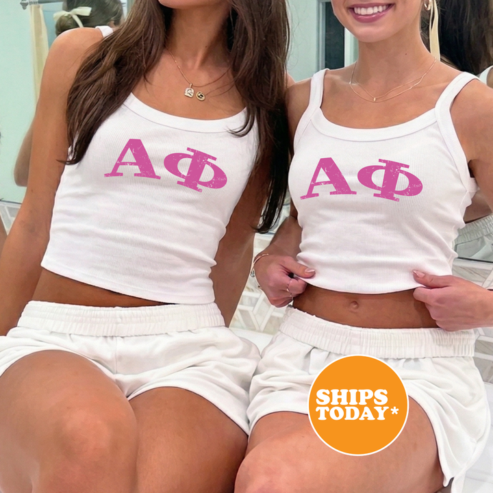 Two women wearing matching white tank tops with the letters "ΑΓΟ" printed on them, posing together in front of a mirror.