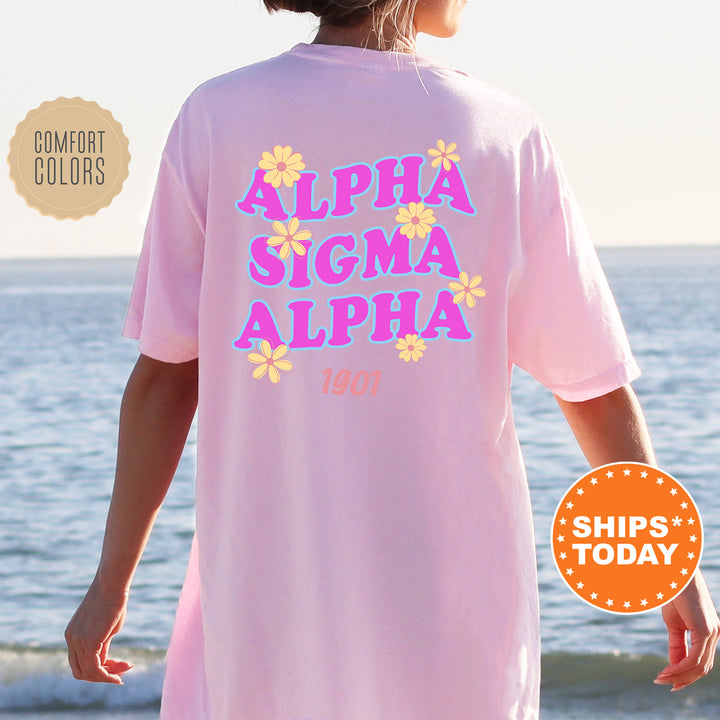 A person wearing a pink t-shirt with the text "ALPA SIGMA ALPHA" printed on it, standing near the ocean.