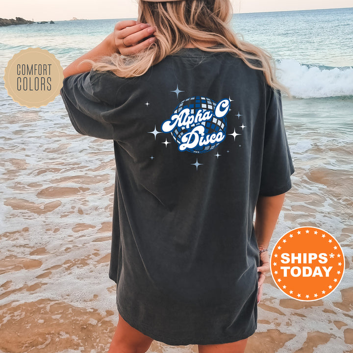 A woman wearing a black t-shirt with a graphic design on the back is standing on a beach, with the ocean and waves visible in the background.
